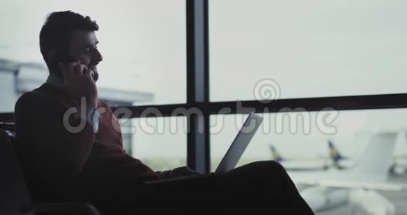 机场的贴身商人正在等待登机牌他用笔记本电脑工作用手机说话他视频的预览图