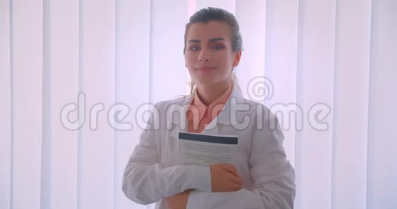 年轻迷人的白种人女医生拿着一本书看着摄像机站着的特写照片视频的预览图