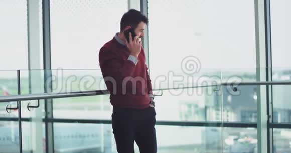 一位年轻的上班族正在打电话他站在一座现代化建筑的大窗户旁聊天视频的预览图