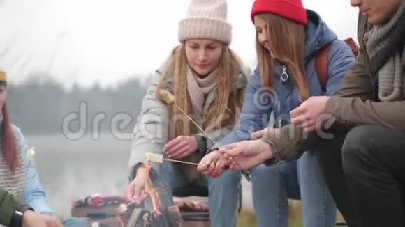 一群快乐的朋友围着篝火在树林里烤棉花糖谈着笑着徒步旅行者视频的预览图