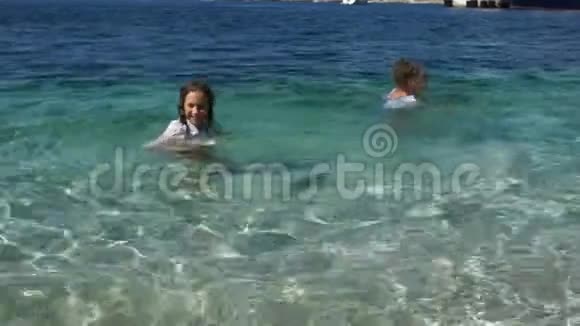 快乐的孩子和孩子一起休息两个孩子一个男孩和一个女孩穿着衣服在绿松石的海水中游泳视频的预览图