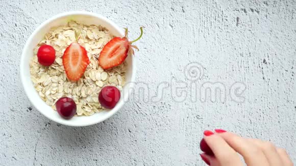 一张厨房桌子的细节照片上面有一杯白色的燕麦片和草莓还有一只手把草莓放在上面视频的预览图