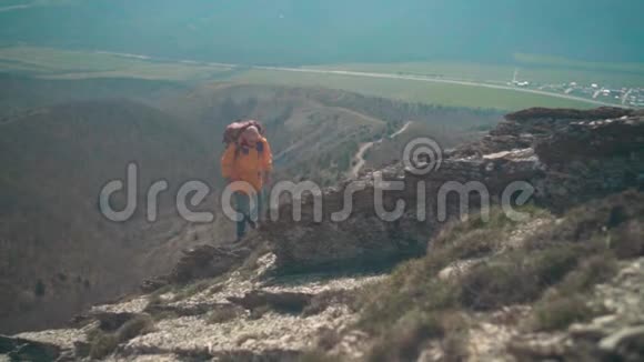 一个穿着黄色夹克眼镜和一个大型旅游背包的人沿着山脊散步欣赏风景视频的预览图