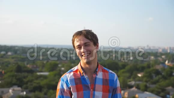 在城市景观背景下坐在屋顶上的年轻快乐男人的肖像英俊的家伙笑着露出喜悦的表情视频的预览图