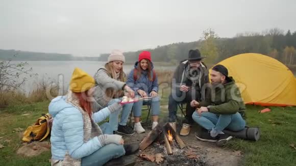 一群快乐的朋友围着篝火在树林里烤棉花糖谈着笑着徒步旅行者视频的预览图