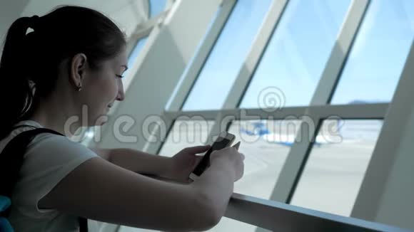 年轻女子正在看手机屏幕等待她在机场的航班视频的预览图