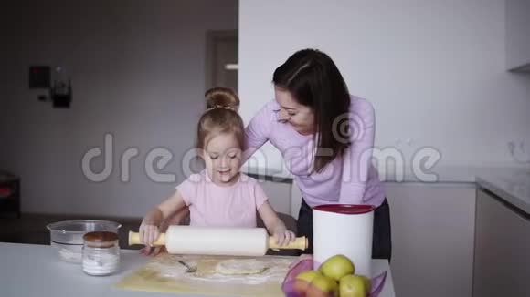 美丽的年轻慈爱的母亲教她可爱的小女儿做饭时用擀面杖擀面团视频的预览图
