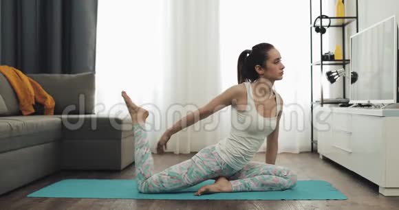 年轻女子在家训练瑜伽坐在垫子上伸展腿部肌肉健康和运动的生活方式视频的预览图