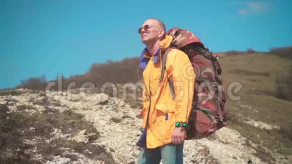 一个穿着黄色夹克眼镜和一个大型旅游背包的人站在山上欣赏着风景视频的预览图