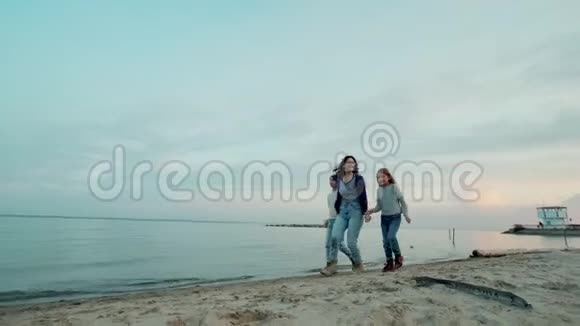 年轻的母亲和她的孩子们在户外玩得很开心孩子们和妈妈在日落时沿着海滨跑步视频的预览图