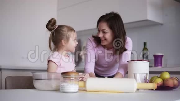 母亲和女儿在面团里放一些面粉妈妈教女儿揉面团现代化明亮的厨房视频的预览图
