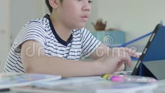 漂亮的亚洲男孩坐在家里的椅子上用平板电脑做作业来找到答案视频的预览图
