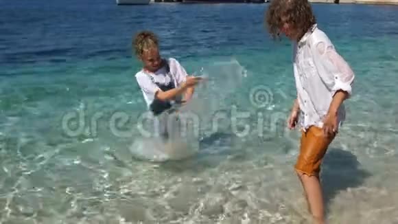 卷曲的男孩和女孩有趣的泼水站在海里的衣服亚得里亚克罗地亚的假日视频的预览图