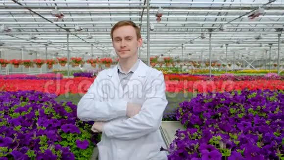 一位年轻的男科学家或农学家穿着一件白色外套在温室里放着花的床的背景下工作视频的预览图