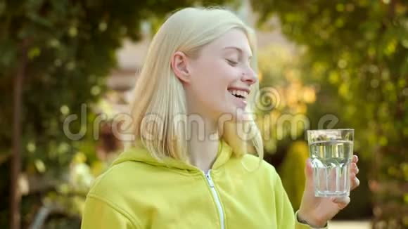 玻璃水的女人的面部肖像年轻女子喝水把金发女孩的画像贴起来视频的预览图