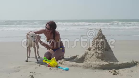 一个女孩正在海边建一座沙堡拥抱一只白狗4K视频的预览图