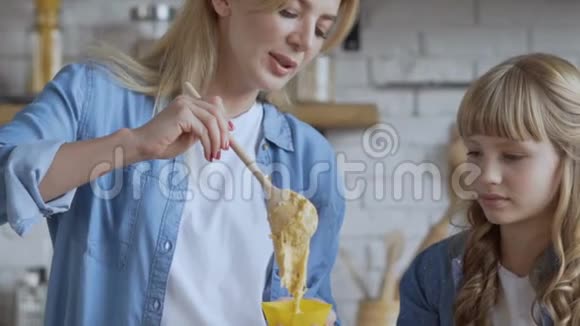妈妈和女儿正在厨房准备纸杯蛋糕妈妈把一个木勺放在面团上以一种硒的形式特写视频的预览图