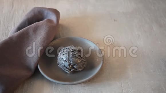 灰色桌子上灰色陶瓷盘子上的黑色冰淇淋女人手把锥子放在冰淇淋上视频的预览图