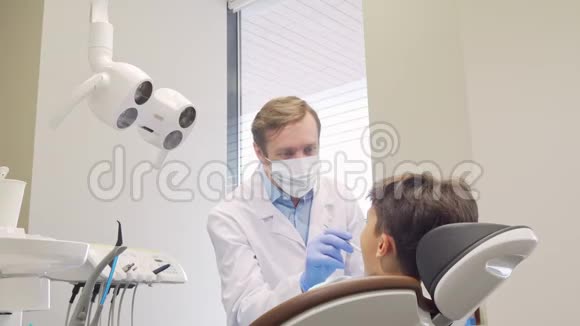 成熟的牙医在检查了他的小病人的牙齿后视频的预览图