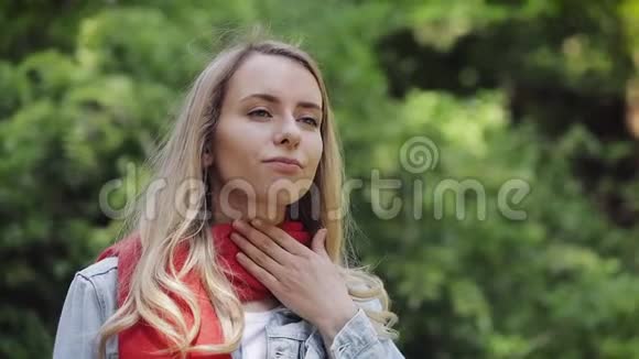 生病的年轻女子戴着红领巾感觉不好喉咙痛站在公园里痛苦视频的预览图