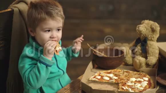 一个男孩在木制背景下吃披萨小男孩把一片披萨隔离在木头上视频的预览图