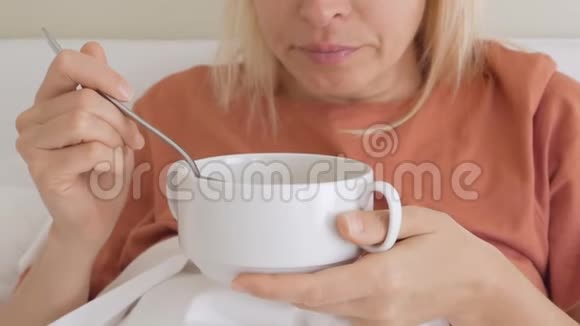 一个女人一张悲伤痛苦的脸坐在白色毯子下的床上吃着一盘汤视频的预览图
