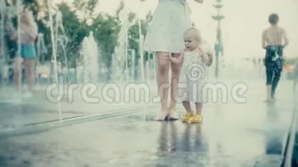 妈妈和她的小宝宝在城市公园喷泉里玩慢动作视频的预览图