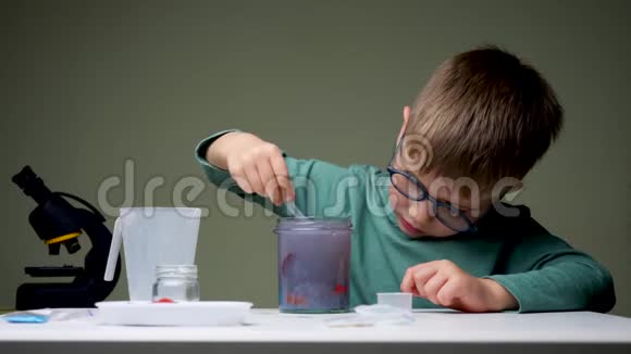 戴眼镜的男孩在做实验年轻的科学家把地衣混合起来做实验学龄前儿童在室内玩耍家庭视频的预览图