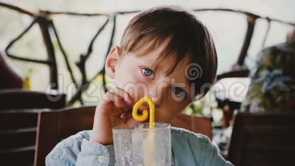 在现代咖啡馆度假时用吸管喝奶昔鸡尾酒的快乐可爱的小欧洲男孩的特写肖像视频的预览图