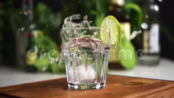 冰块落在苏打水或矿泉水中以食物为背景缓慢运动玻璃上的石灰片视频的预览图