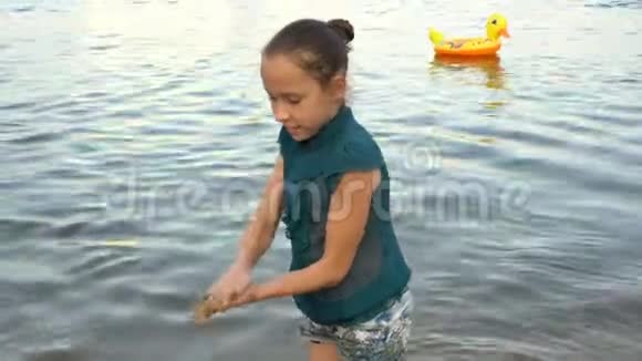 日落时分一个小女孩在海滩上玩耍在平静的水背景下建造了一座沙塔肖像关闭视频的预览图