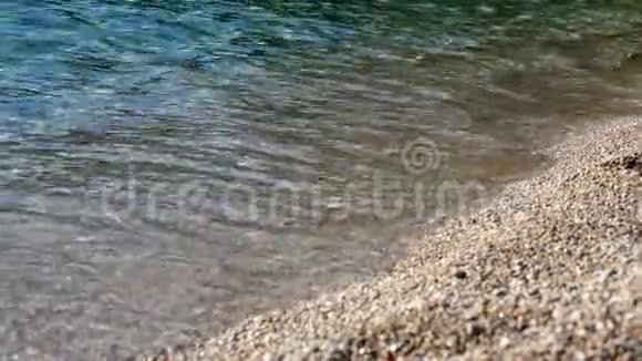 特写镜头软波浪白色泡沫被冲到岸上在卵石海滩上美丽的多种颜色的圆海卵石视频的预览图