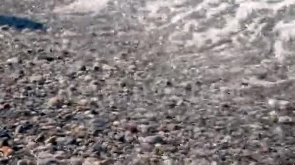 特写镜头软波浪白色泡沫被冲到岸上在卵石海滩上美丽的多种颜色的圆海卵石视频的预览图