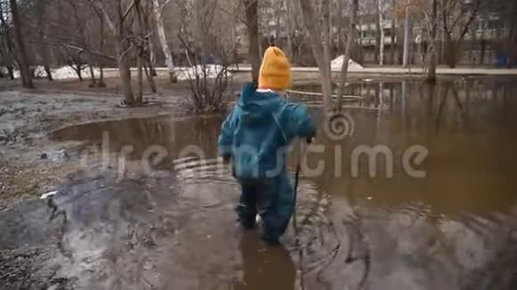 一个小孩子走在一个大水坑里手里拿着一根棍子在春天视频的预览图