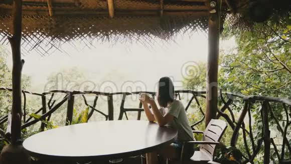 美丽的背景拍摄年轻快乐的旅游妇女享受早晨咖啡在惊人的热带森林酒店露台视频的预览图