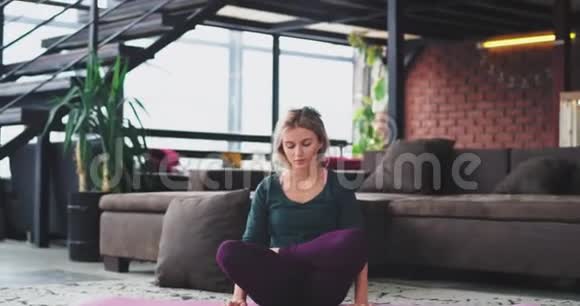 硬瑜伽姿态金发女郎早上在家客厅练习她站在手里有一个视频的预览图