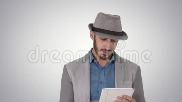 英俊的微笑阿拉伯男子戴着帽子走路和使用平板电脑的梯度背景视频的预览图