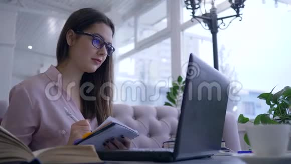 在电子教育期间学生女孩用书和笔记本电脑坐在桌子旁写笔记视频的预览图