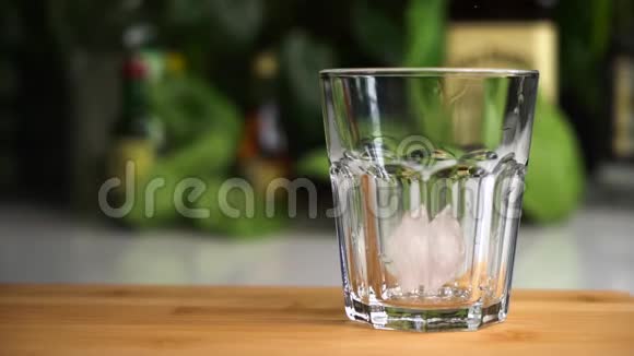 冰块的缓慢运动落在木桌上的玻璃支架上鸡尾酒概念视频的预览图