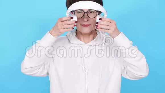 戴着眼镜和白色毛衣的中年妇女用白色背景耳机听她最喜欢的音乐视频的预览图