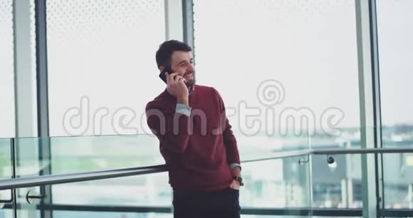 一个漂亮的男人在一个商务大楼里在他的智能手机上说话旁边是一个大窗户视频的预览图