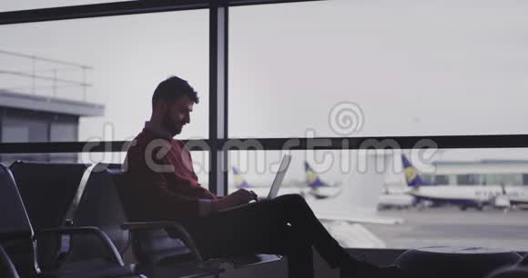 在机场的椅子上商人在他的笔记本上打字直到他等待飞行他非常高兴和享受视频的预览图