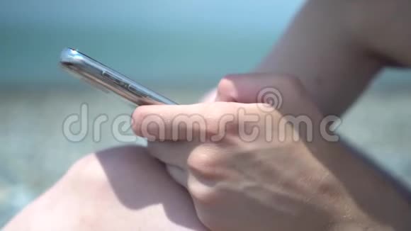 在海滨抽象背景下年轻女性使用智能手机的特写上网冲浪视频的预览图