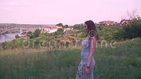 年轻女子在绿树草河桥村屋自然的背景下向前看视频的预览图