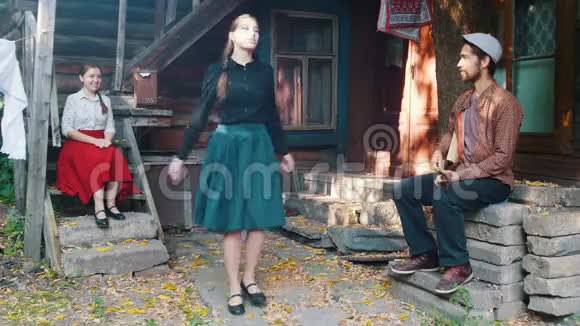 一个漂亮的女人在乡间别墅附近的音乐旁跳舞一个男人在演奏巴拉莱卡视频的预览图