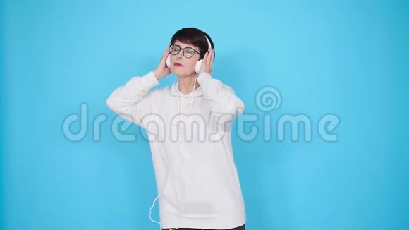 戴着眼镜和白色毛衣的中年妇女用白色背景耳机听她最喜欢的音乐视频的预览图