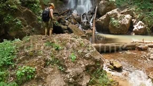 一位戴草帽和背包的男性旅行者在雄伟的背景下爬上岩石的空中景色视频的预览图