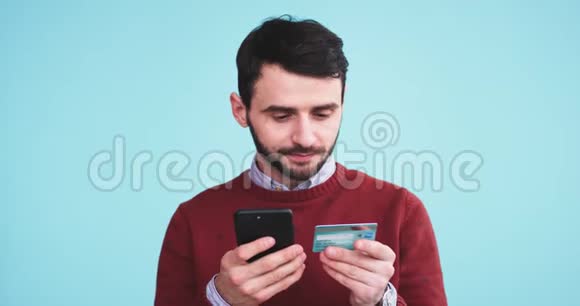塞里奥斯曼使用他的智能手机和信用卡在一个蓝色背景墙的工作室进行在线交易视频的预览图