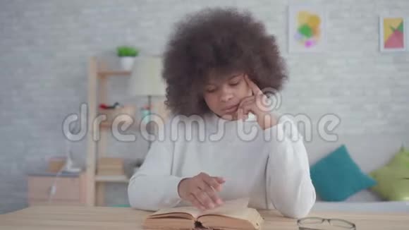 有非洲发型的美国黑人妇女在桌旁看书的肖像视频的预览图