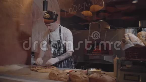 熟练的皮萨约洛正在玻璃后面的现代餐厅厨房做披萨穿着厨师制服的年轻人视频的预览图